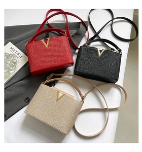Close-up of sequin shoulder bags in red, black, and gold with gold V-shaped metal buckles