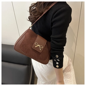 Detail of a brown leather bag featuring a suede texture and gold bow metal buckle