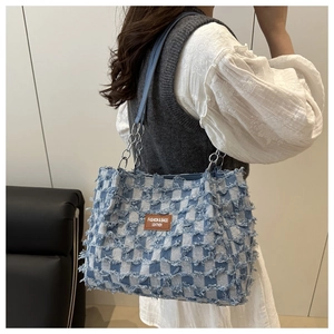 Detail of blue and white checkered tote bag with frayed edges and brown leather logo tag