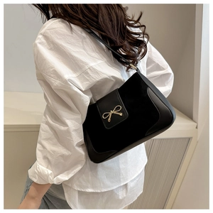 Detail of black crossbody bag featuring gold bow buckle and leather texture contrast