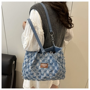 Detailed view of denim tote bag with frayed edges, leather tag and silver chain strap