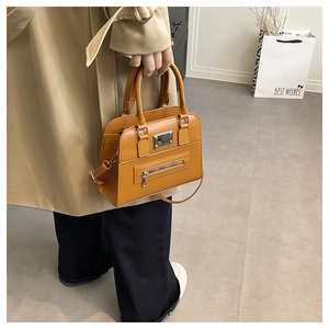 Detail of a ginger yellow faux leather tote bag with metal hardware and crossbody strap