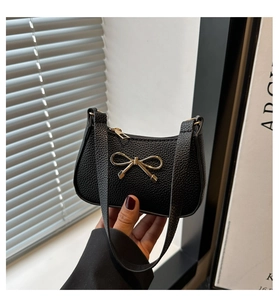 Close-up of black lychee grain leather handbag with gold bow ornament and zipper