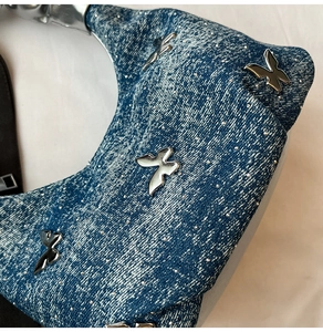 Detail of blue washed denim fabric with metallic silver butterfly 3D accents on shoulder bag