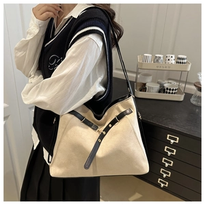 Detail of cream tote bag featuring black leather strap and gold metal buckle accents