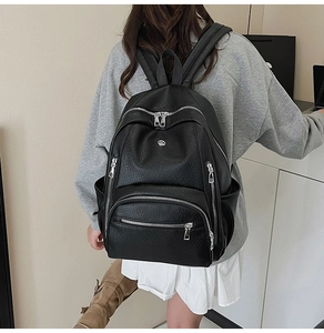 Detail of black pebbled leather backpack showing multi-zipper pockets and metal logo