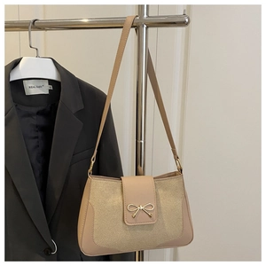 Detail of beige shoulder bag with gold bow ornament hanging on a metal hanger