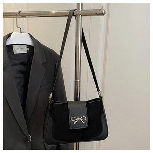 Detail of black suede shoulder bag featuring a metallic bow clasp and sleek leather strap