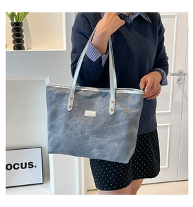 Dettaglio della borsa tote grigia marmorizzata con etichetta fashion argento e manici