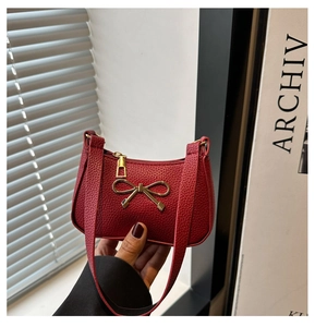 Detail of red pebbled leather handbag featuring a golden bow accent and zipper