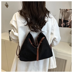 Detail view of black canvas tote bag with brown leather straps worn on shoulder