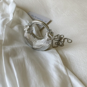 Detail of silver half-moon evening bag with metallic pleated texture and chain strap