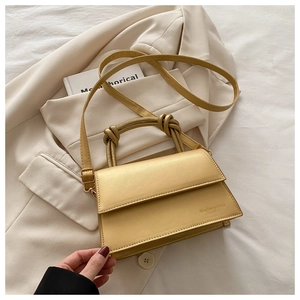Detail of light yellow leather handbag featuring a knotted handle and embossed logo text