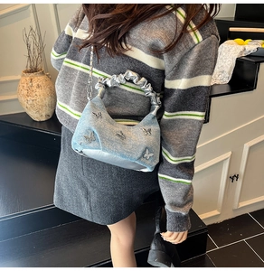Close-up of denim shoulder bag with silver butterfly charms and metallic pleated handle