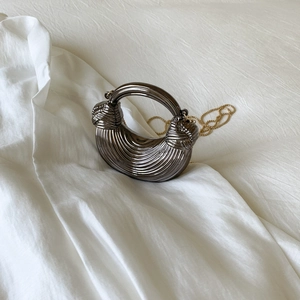 Detail view of semi-circular metallic handbag with twisted handle and gold chain strap