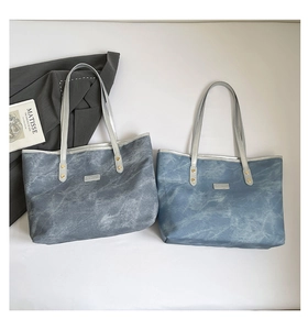 Dettaglio di una borsa tote grande con trama denim lavato e bordi metallici argentati