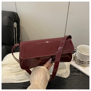 Détail d'un sac à bandoulière en cuir verni bordeaux brillant avec rabat magnétique