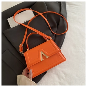 Detailed view of an orange quilted crossbody bag on a black blazer with an arts book