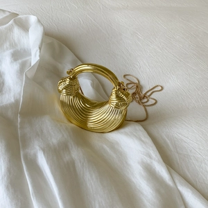 Detail of golden acrylic hobo bag featuring pleated texture and metal chain strap
