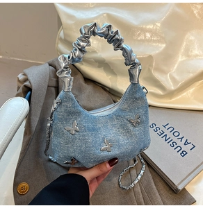 Close-up of denim shoulder bag featuring silver butterfly buckle and metallic handle