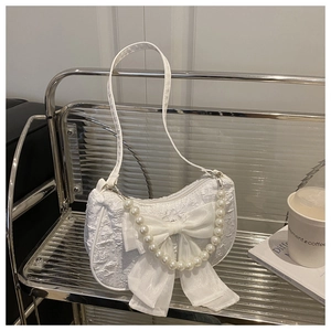 Detail der weißen Plissee-Handtasche mit großer Schleife und eleganter Perlenkette