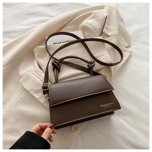 Detail of dark brown leather crossbody bag with knot handle on a cream blazer