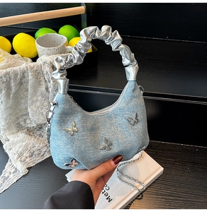 Detail of light blue denim handbag featuring silver butterfly charms and pleated strap