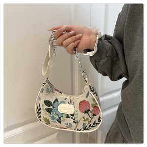 Close-up of floral embroidery on beige hobo bag with silver chain and leather handle