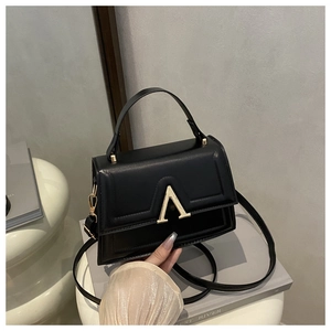 Detail of black glossy leather square bag with distinctive gold metal V-shape buckle