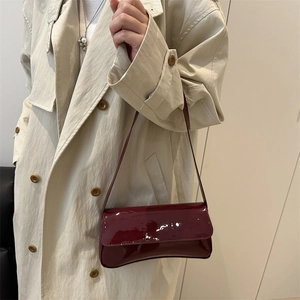 Sac sous le bras minimaliste en cuir verni bordeaux porté avec un trench-coat beige chic