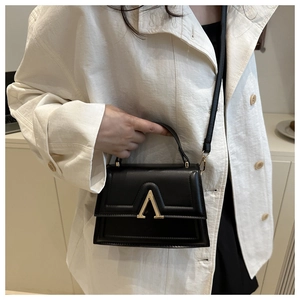 Detail of black crossbody bag with gold V-shape clasp on ivory trench coat