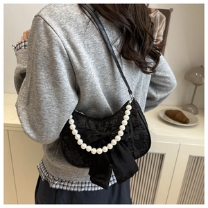 Detail of black lace shoulder bag featuring large silk bow and decorative pearl handle