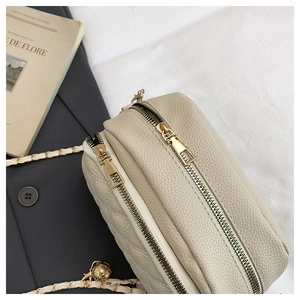 Detail of cream quilted crossbody bag featuring dual gold zippers and chain strap