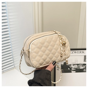 Detailed view of beige quilted bag with gold chain strap and spherical metal pendant