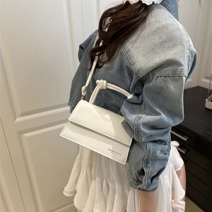 White minimalist leather messenger bag featuring a unique knotted handle and embossed text
