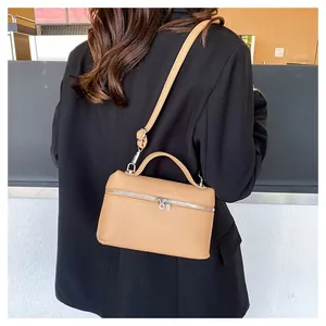 Crossbody view of a textured light brown leather square bag on a black blazer