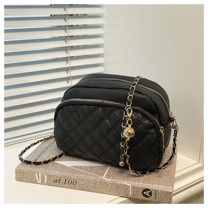 Detail of black quilted leather crossbody bag with dual zippers and gold ball chain strap