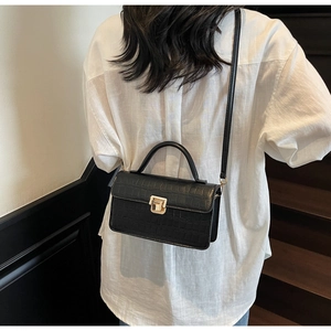 Back view of black croc-embossed square bag with gold buckle on a model in a stairwell