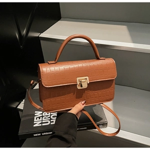 Detail of brown crocodile pattern leather bag with vintage gold square lock and handle