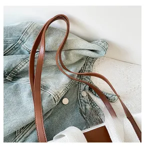 Detail of long brown leather shoulder strap on a white canvas tote bag with contrast stitching