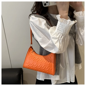 Detail view of a bright orange crossbody bag featuring a classic quilted diamond pattern