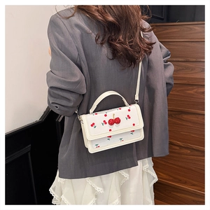 Detail of white mini square bag with red cherry prints and 3D cherry ornament