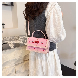 Detail of pink crossbody bag with red cherry pattern and 3D cherry charm on a model
