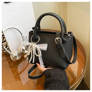 Detail of black lychee grain leather bucket bag with lace bow and pearl pendant charm