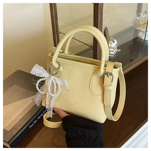 Detail of yellow pebbled leather bucket bag with fashion logo and pearl lace bow charm