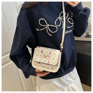 Detail of white mini crossbody bag featuring floral bear print and gold logo plaque