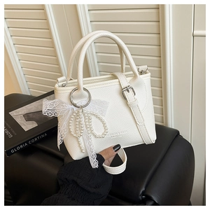 Détail du sac seau blanc avec texture litchi, nœud en dentelle et breloque perle