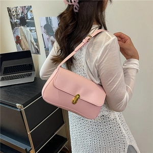 Pink faux leather shoulder bag with gold clasp shown on model in a modern room