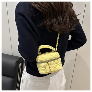 Détail d'un sac cosmétique jaune matelassé avec bandoulière chaîne sur un modèle