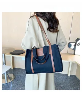 Model wearing a large canvas tote bag in black and brown against a minimalist interior